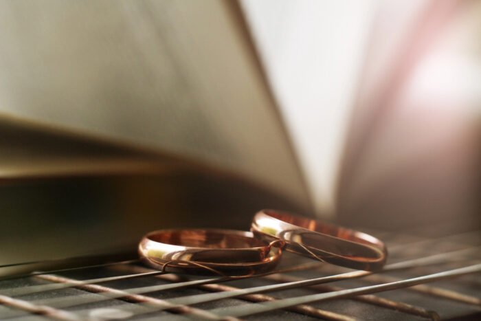 Two gold wedding rings placed on a reflective surface with a blurred open book in the background, symbolizing divorce and legal strategies.